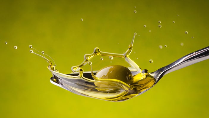 Olive falls into a spoon with olive oil splashing.