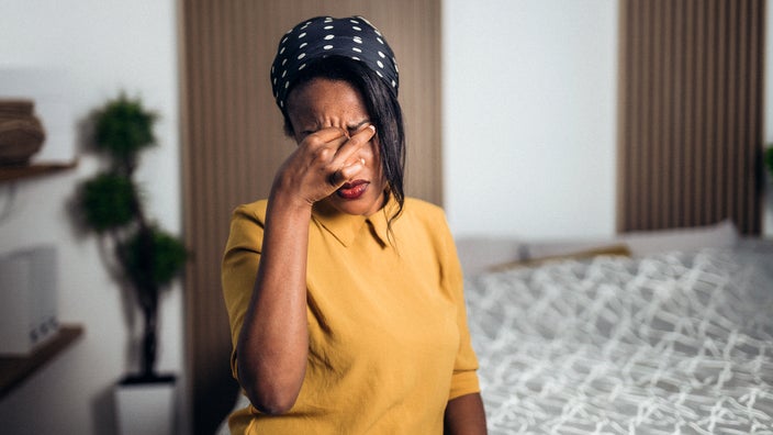 A woman is having a headache while sitting on her bed. Headaches are one of the symptoms of low ferritin levels.