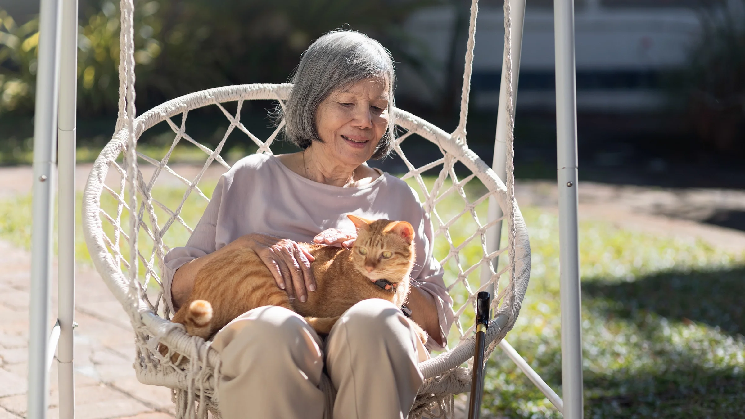 Older woman sitting on an outdoor swinging chair with her cat.