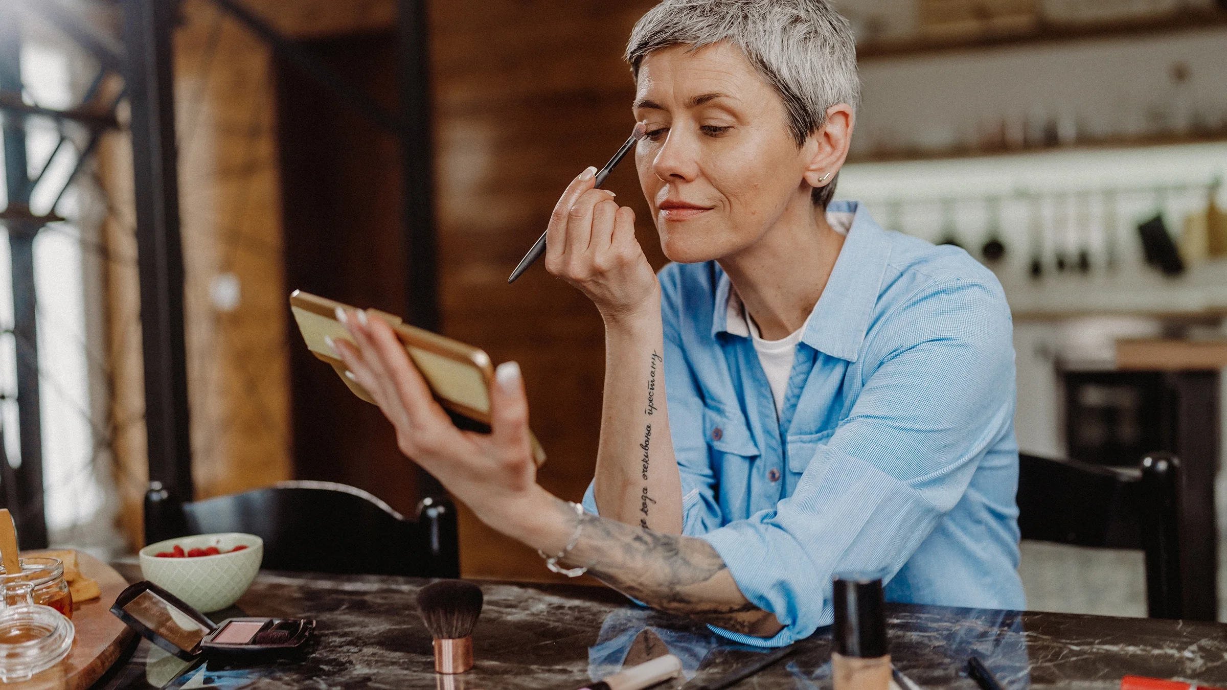 A person applies makeup while sitting at the dining table.