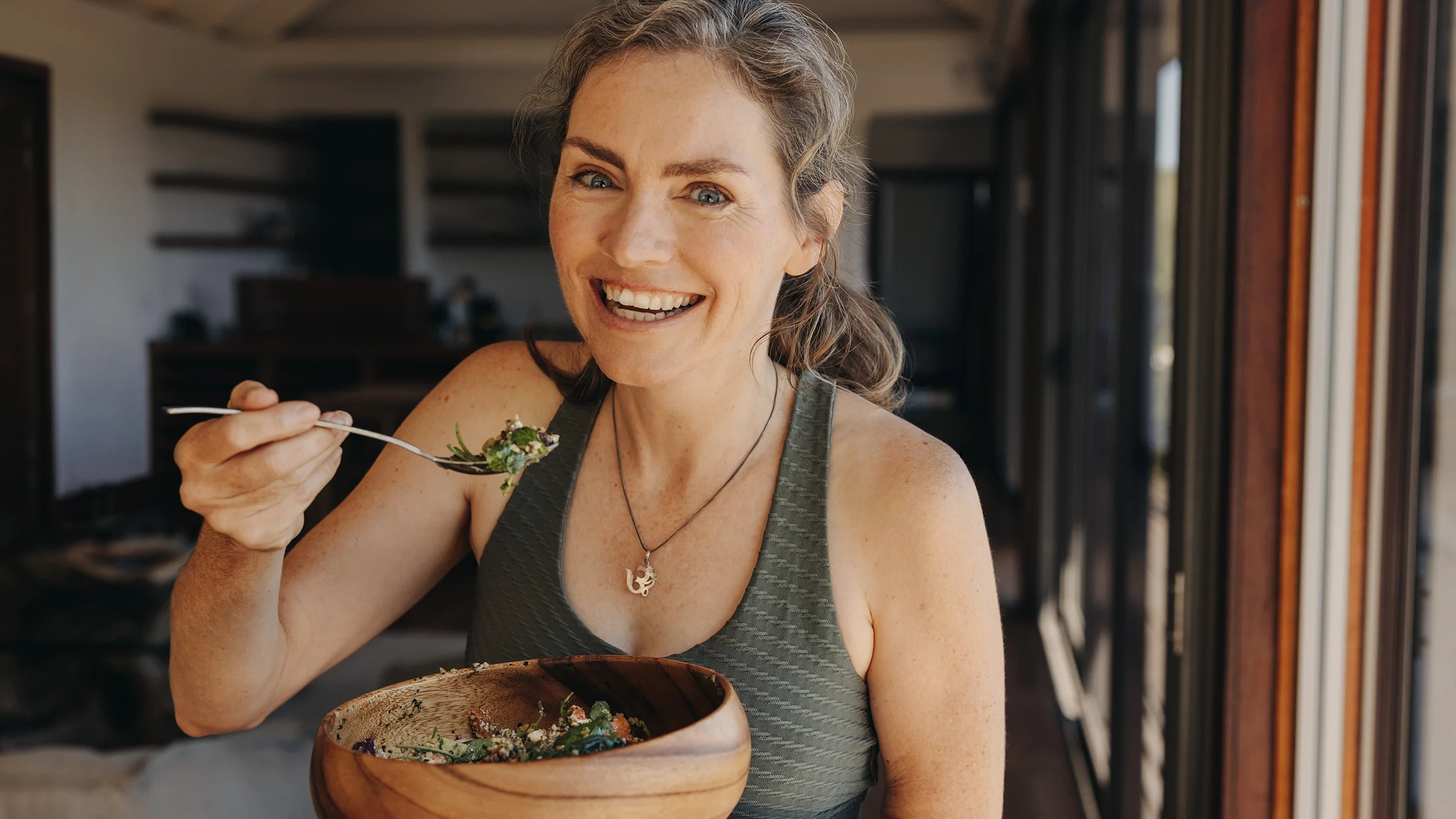 Woman eating a salad from a wooden bowl.
