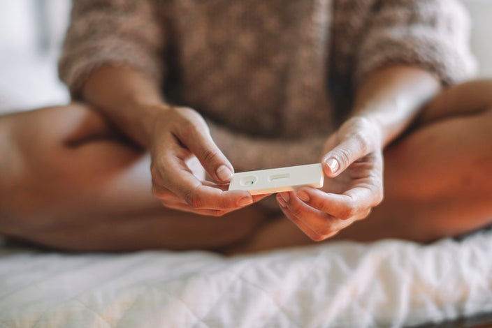 Close-up of a woman sitting cross legged on a bed with an at home fertility test in her hands.