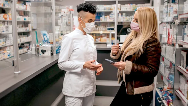 Pharmacies: customer showing phone to pharmacist 1290601847
