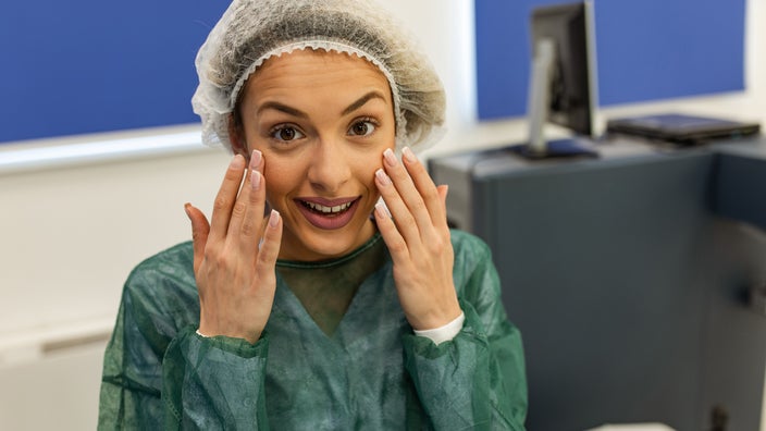 Young woman preparing for laser eye surgery. She has on a paper hair net to hold her hair back and a green paper gown over her clothes for protection.