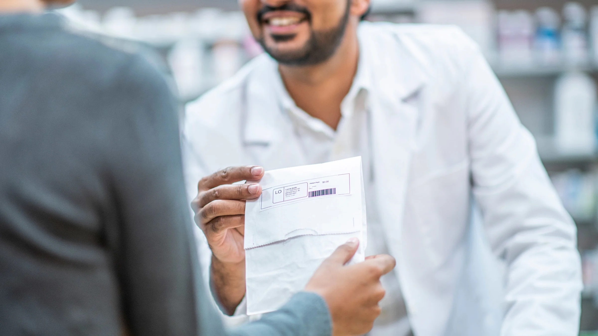 Close up of a pharmacist handing their customer a prescription bag.