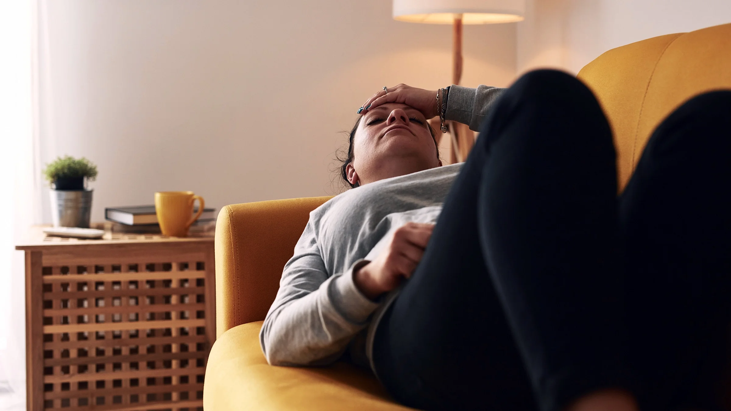 A woman lies on the couch in discomfort as she experiences nausea.