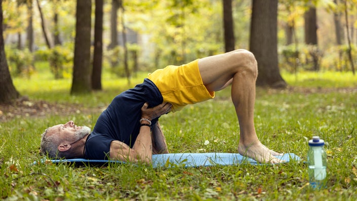 A man is doing a bridge exercise on a yoga mat outdoors.