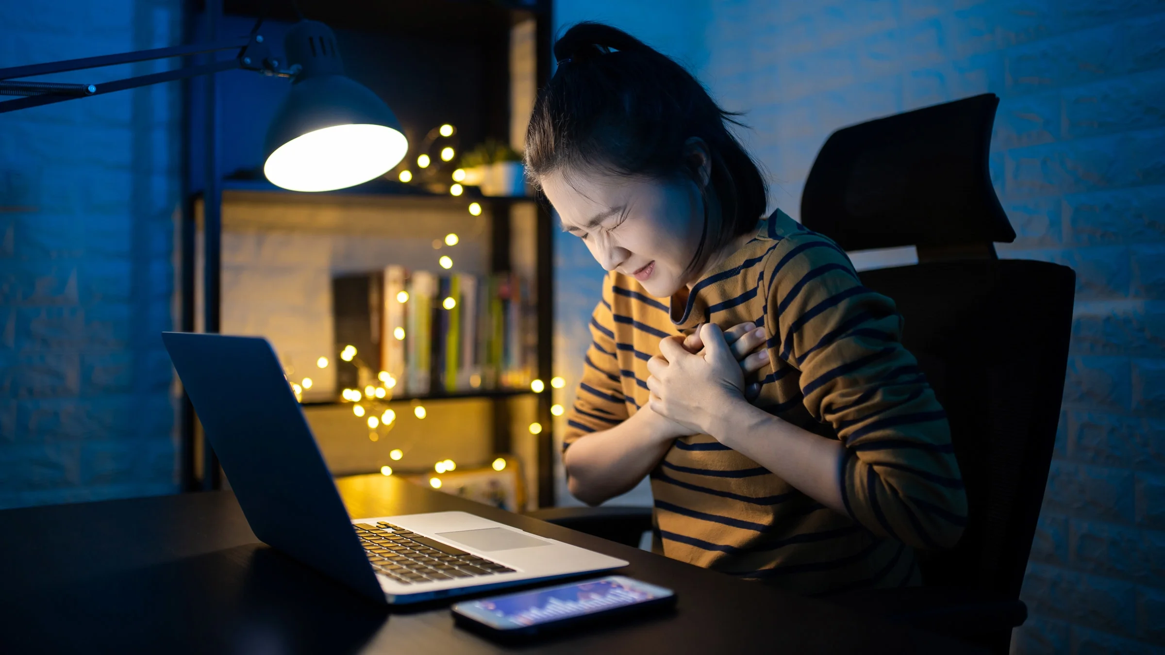 A person experiencing heartburn and clutching their chest while working on laptop.