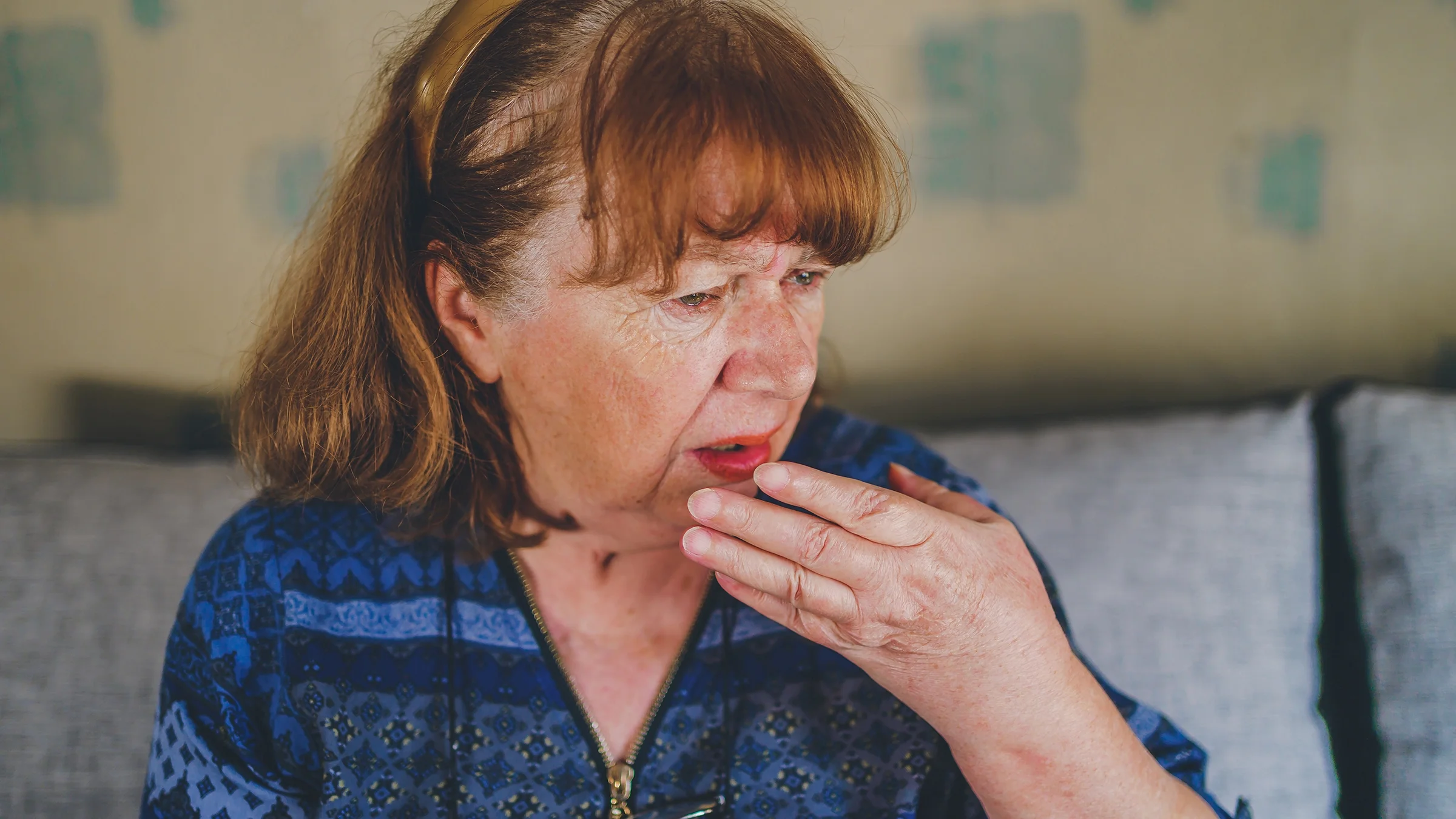 Close-up portrait of an older woman covering her mouth.