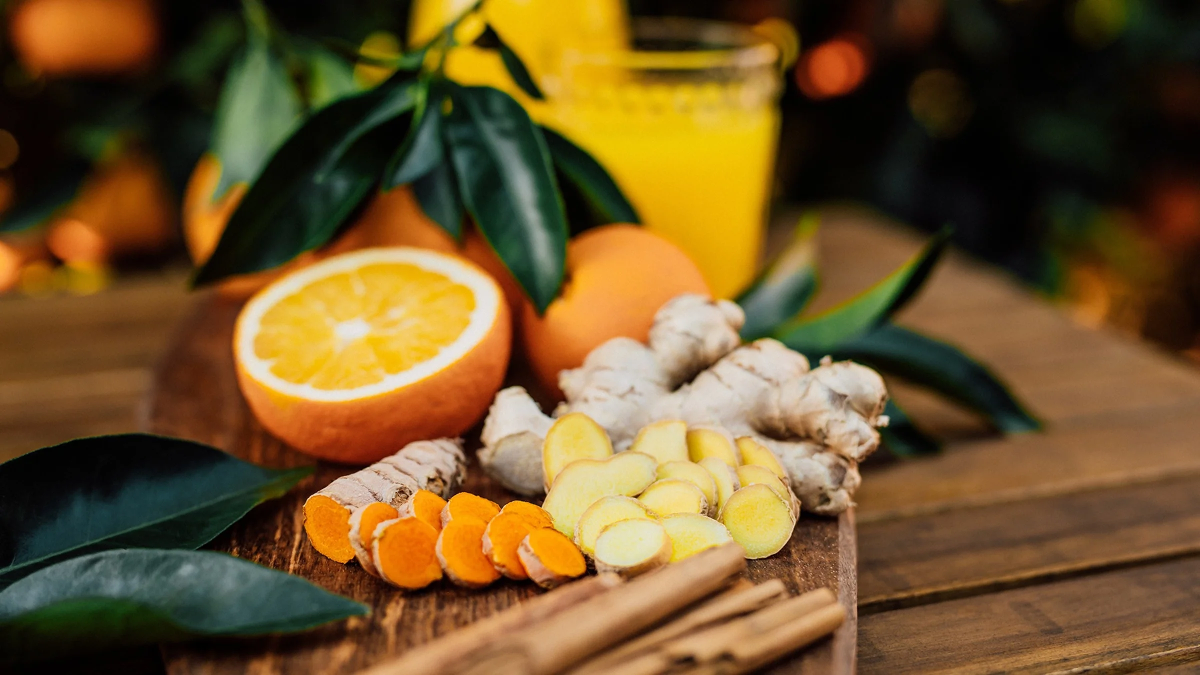 Fresh raw turmeric and ginger root with oranges cut in half and cinnamon sticks surrounding it on a nice wooden serving plate on a wooden table.