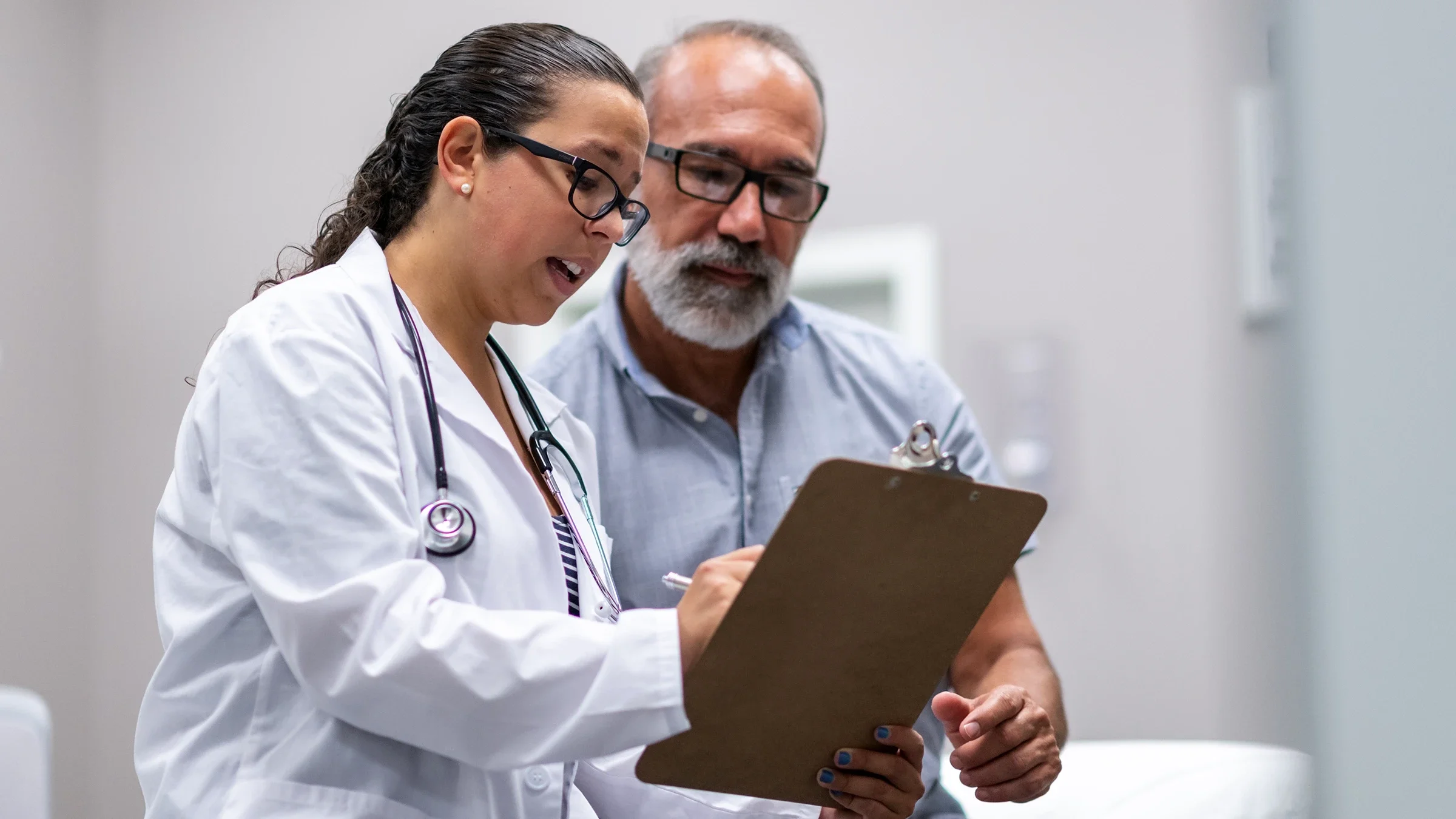 A healthcare professional consults with an older, male patient with a beard.