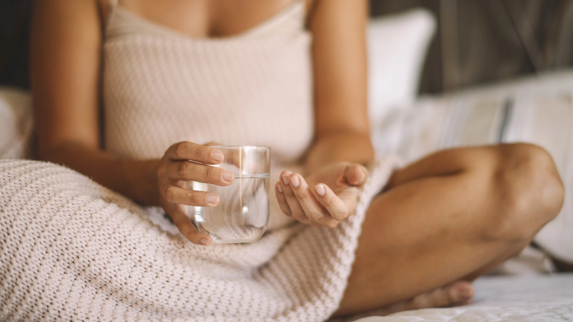 A cropped shot of a person taking a pill in bed.