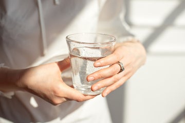Cropped close-up shot of a woman holding a glass of what with the sun shinning on her hands.