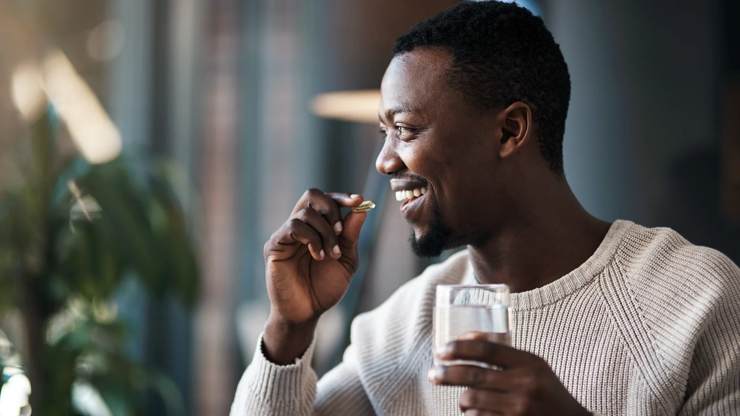 A man is taking his medication with water in his living room.
PeopleImages/iStock via Getty Images Plus