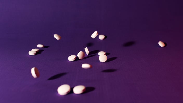 Pink pills are scattered on a purple surface.