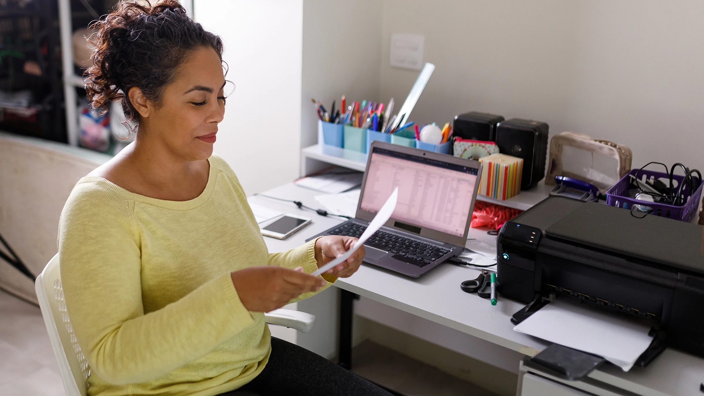 A woman sits at her desk reading a computer printout. 