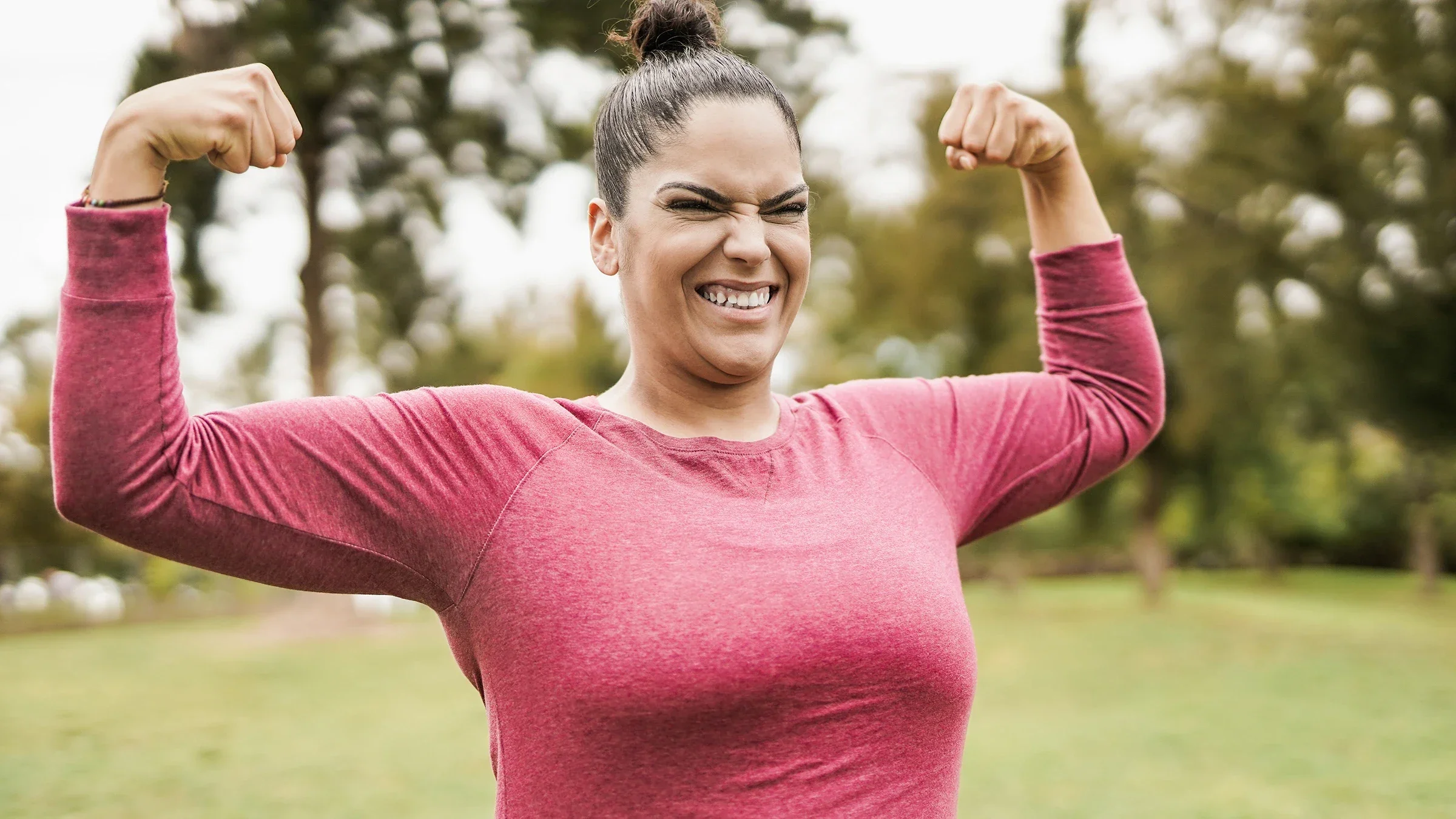 Woman flexing outside after working out. She is wearing a pink long sleeve workout shirt.
Sabrina Bracher/iStock via Getty Images
