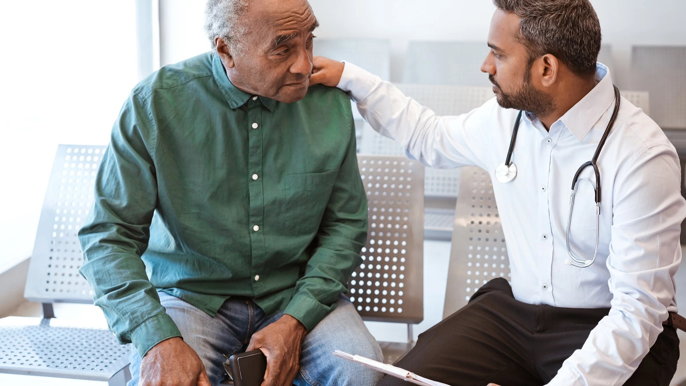 Male doctor consoling a male patient in the lobby.