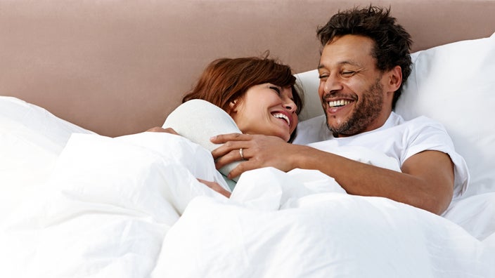 A couple smile as they lie together in bed. 