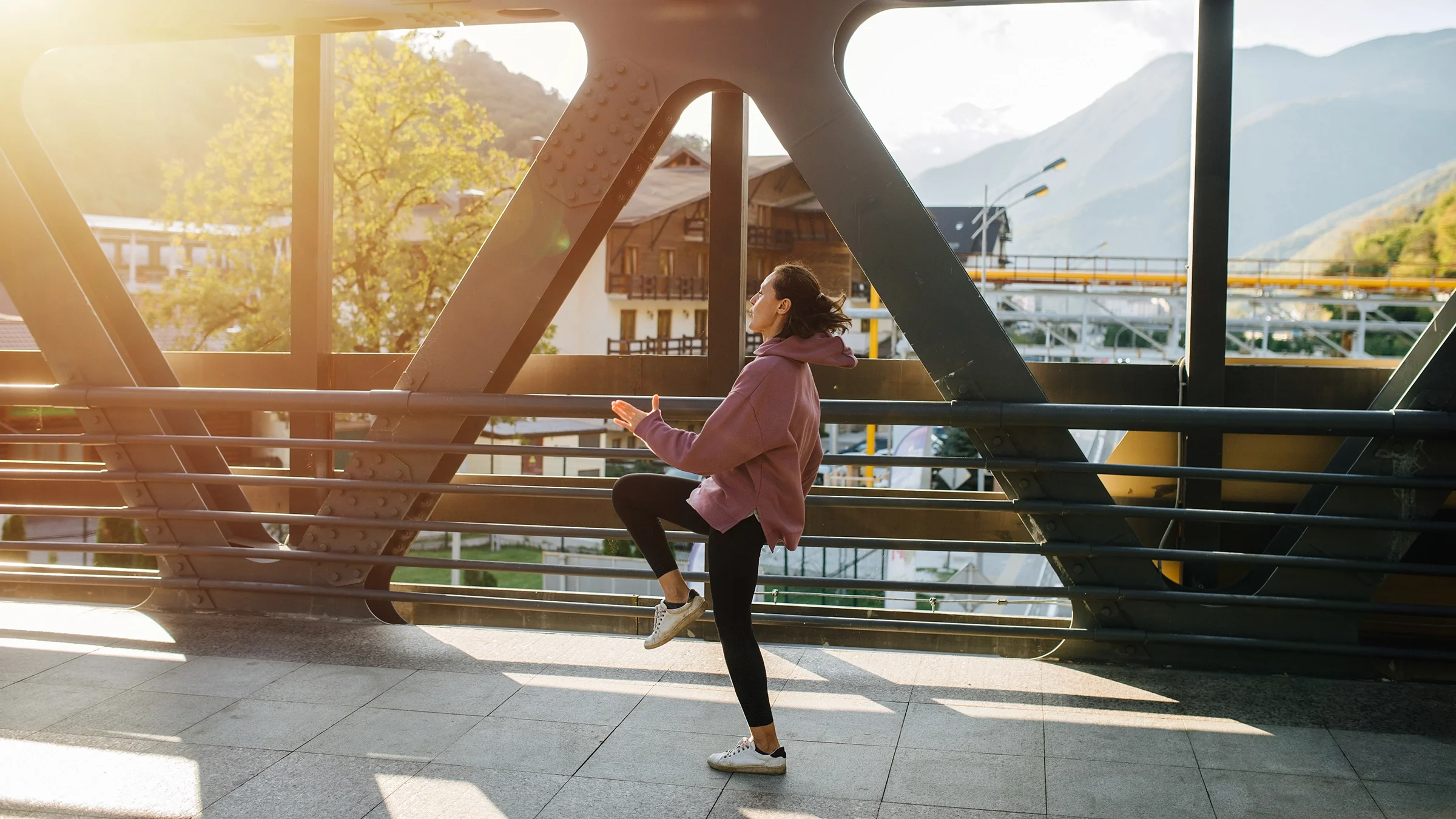 A woman does a high-knee exercise outdoors on a bridge.