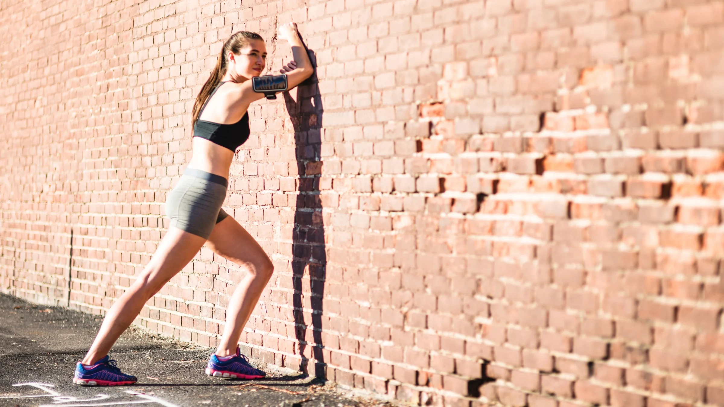 A person doing a catch stretch against a brick wall.