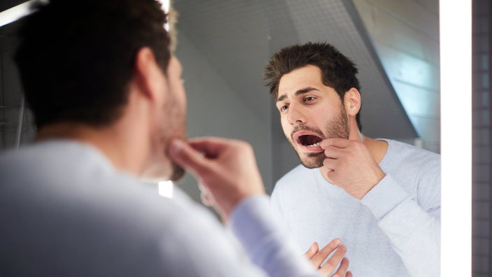 A man who lost a filling looks at his tooth in the mirror.