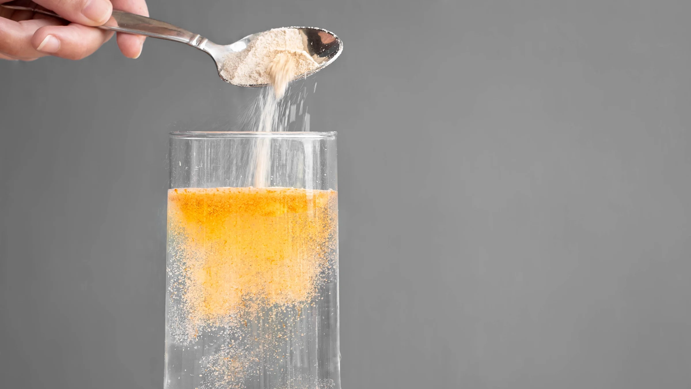 Close-up shows powder supplement being poured into a glass of water.