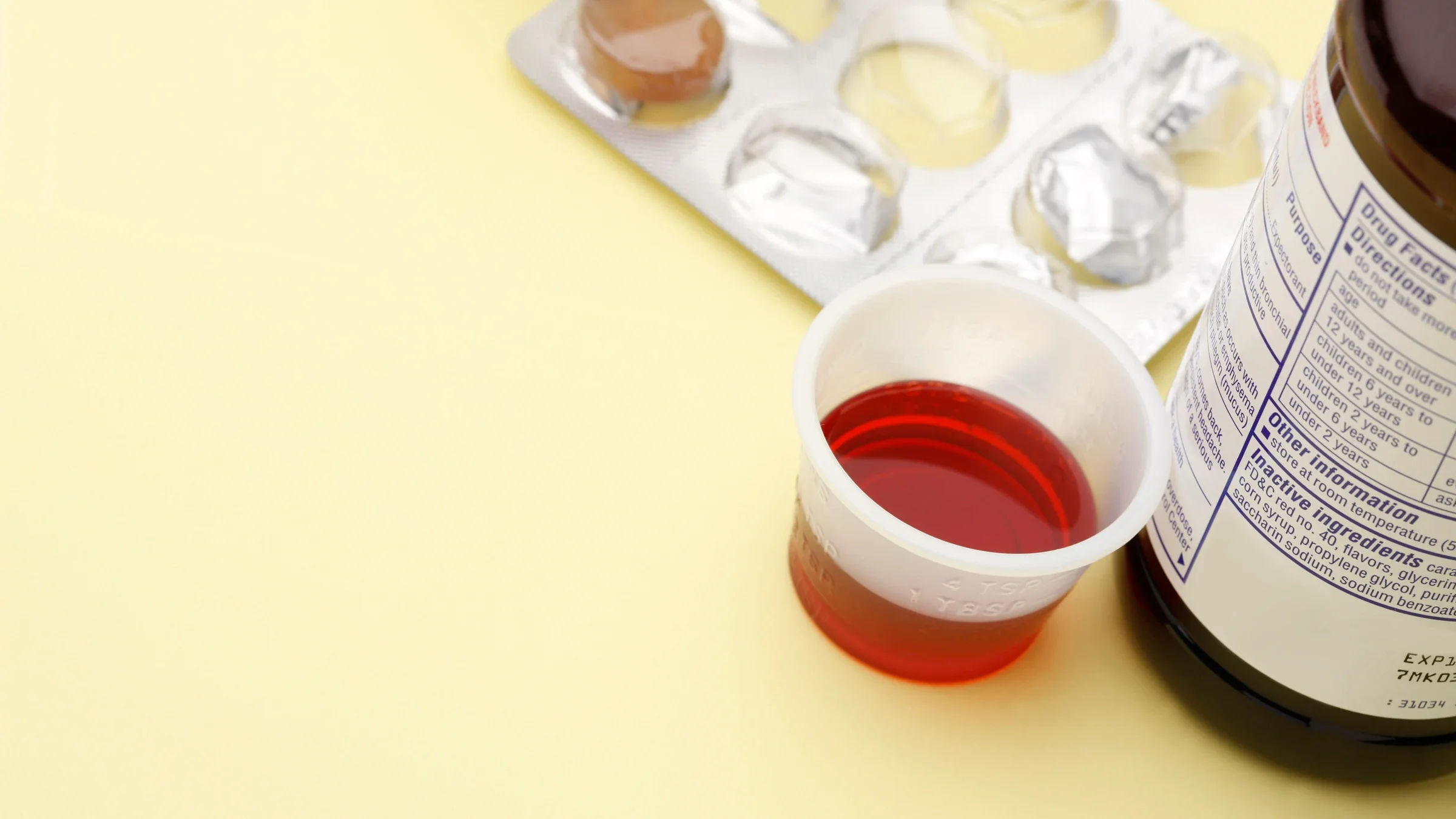 A liquid medicine cup and cough drop package sit before a yellow background.
duckycards/iStock via Getty Images