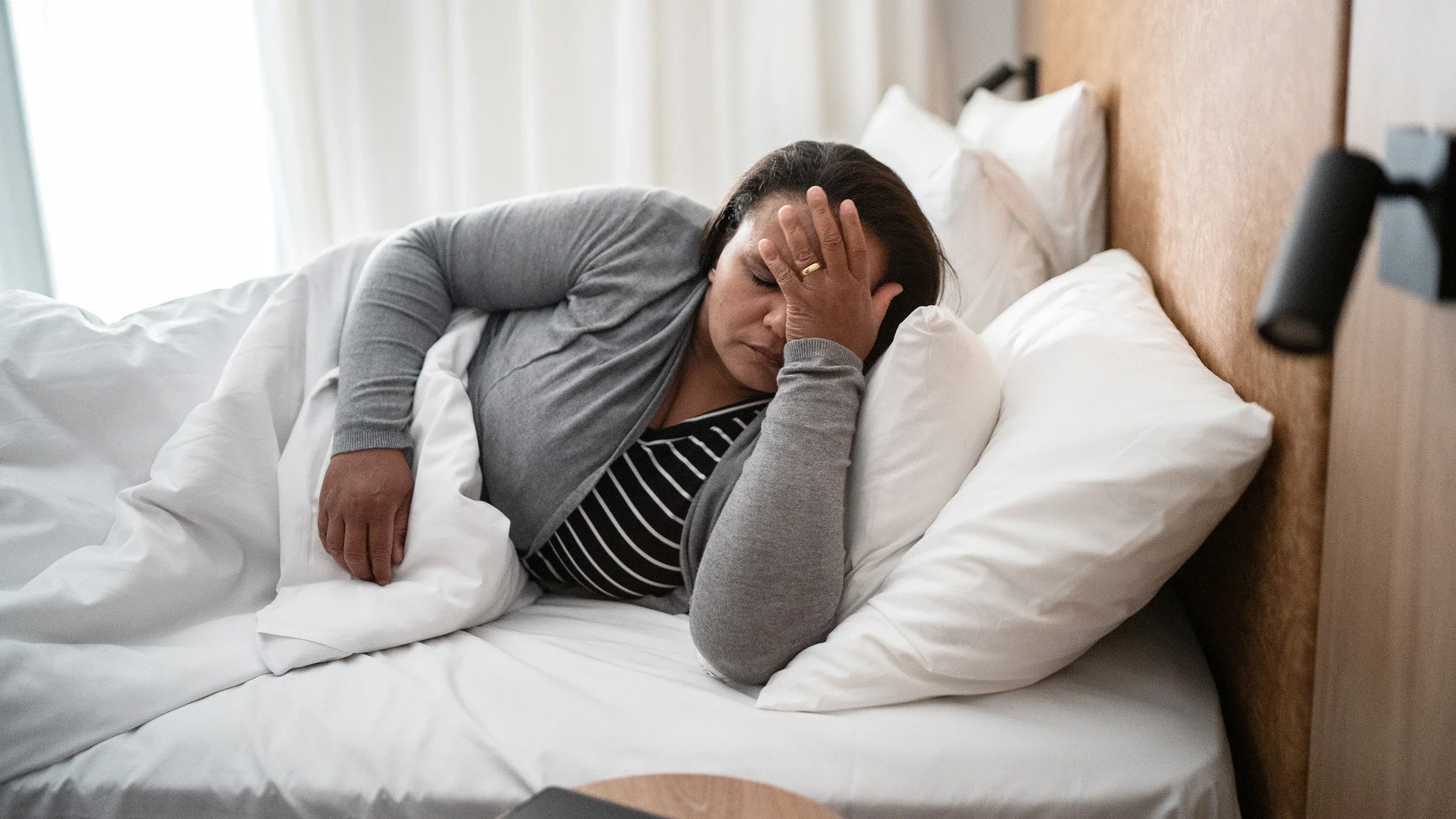 A woman clutches her forehead in discomfort as she lies in bed with a headache.
FG Trade/E+ via Getty Images 