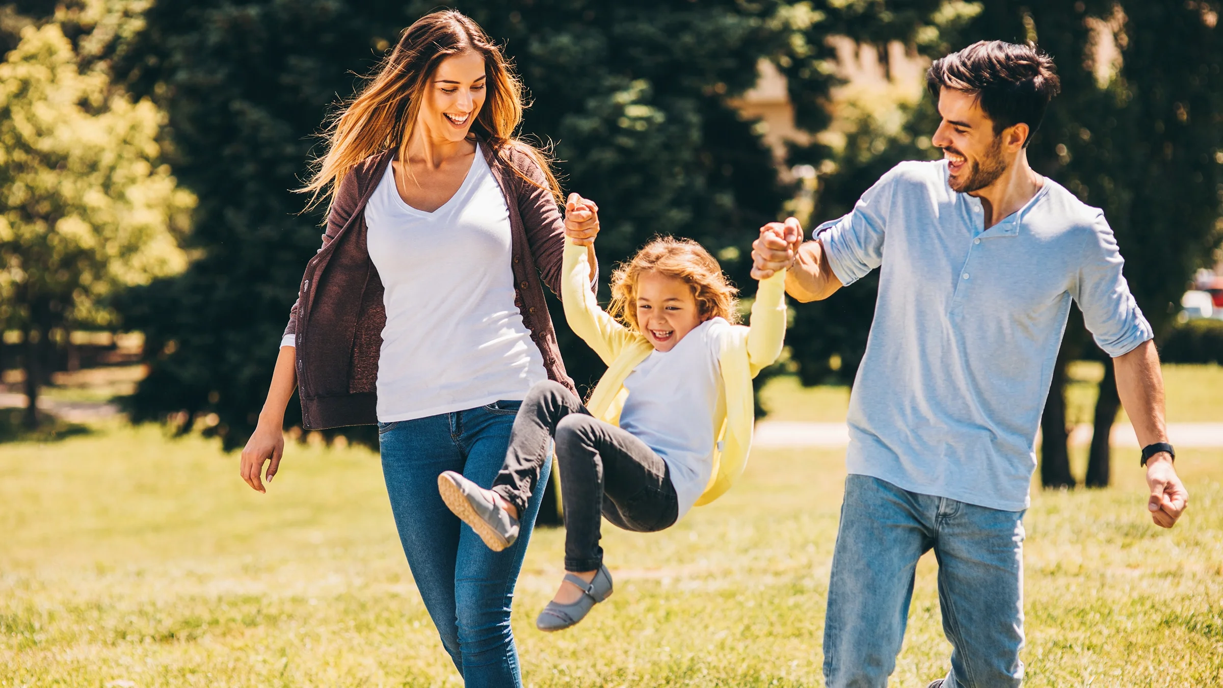 Parents swinging their little girl around in an open field.