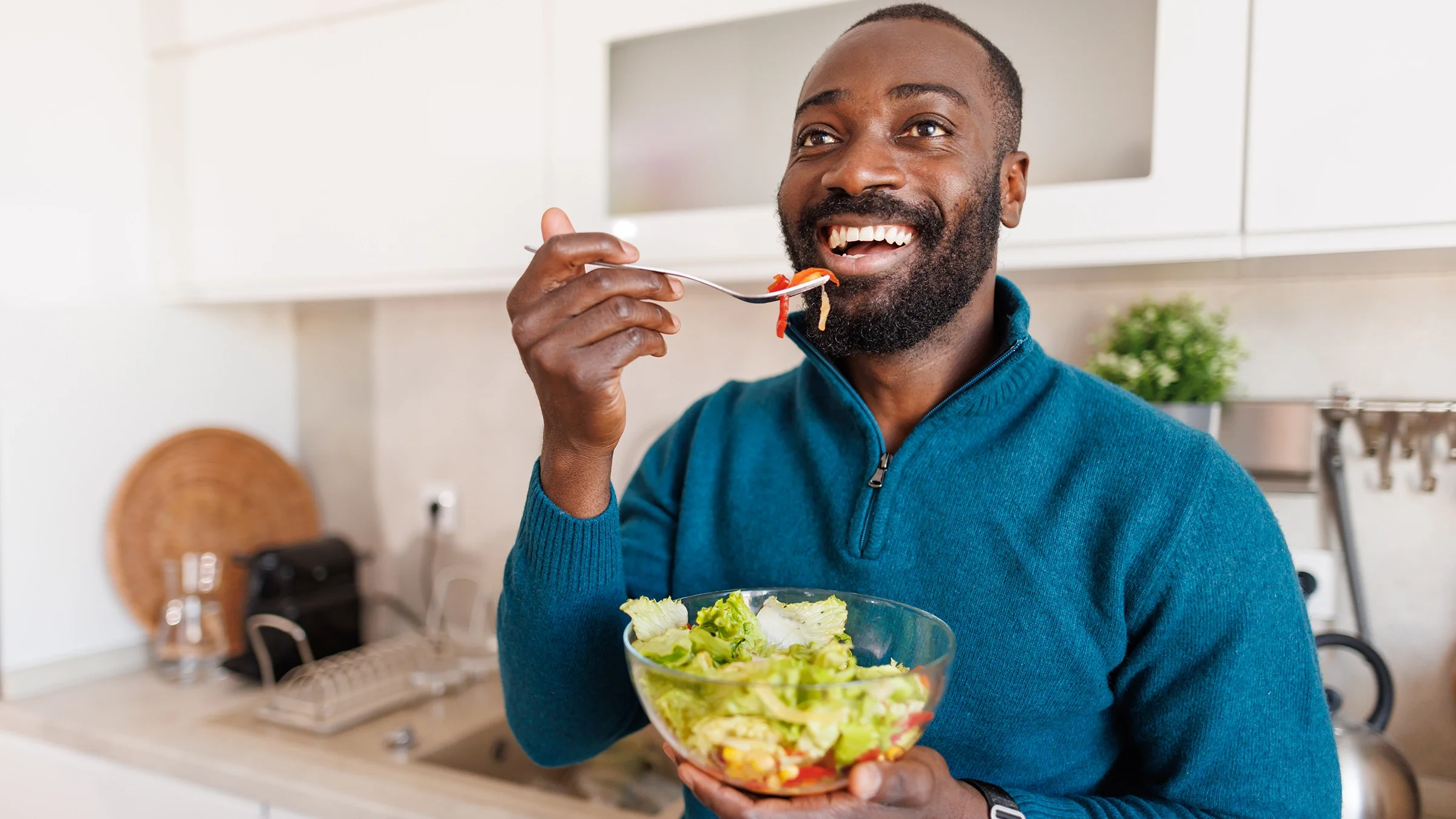 A man with a beard and a blue sweater savors a healthy salad.