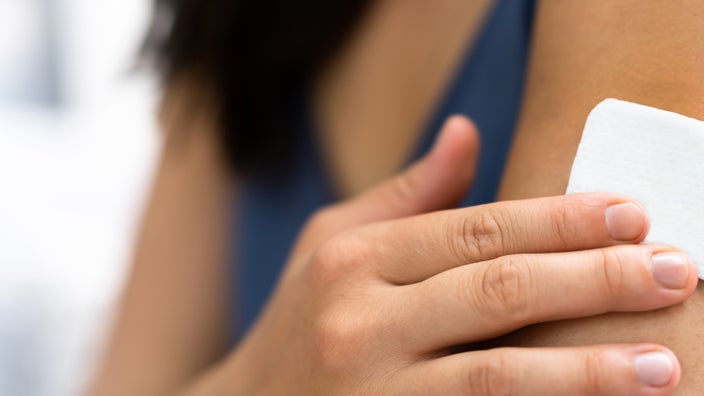 A woman is putting a nicotine patch on her arm in a close-up.