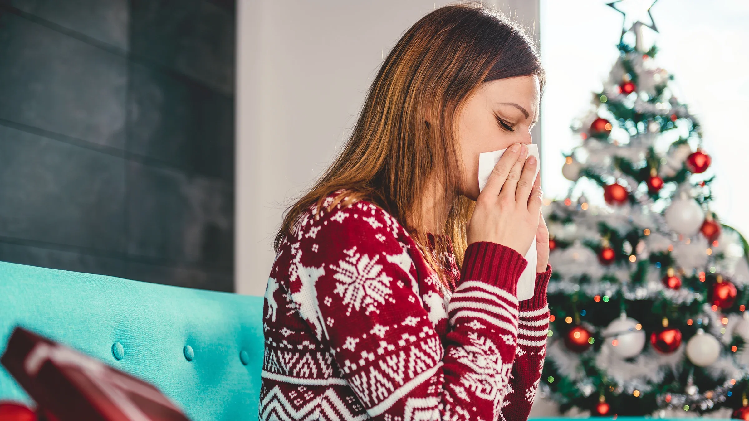 Women sitting next to a Christmas tree blow their nose. Christmas trees contain allergens that can make your nose itch and even give you a rash. 
Kerkez/iStock via Getty Images Plus