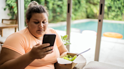 A woman looks at her phone while eating a salad.
FG Trade/E+ via Getty Images