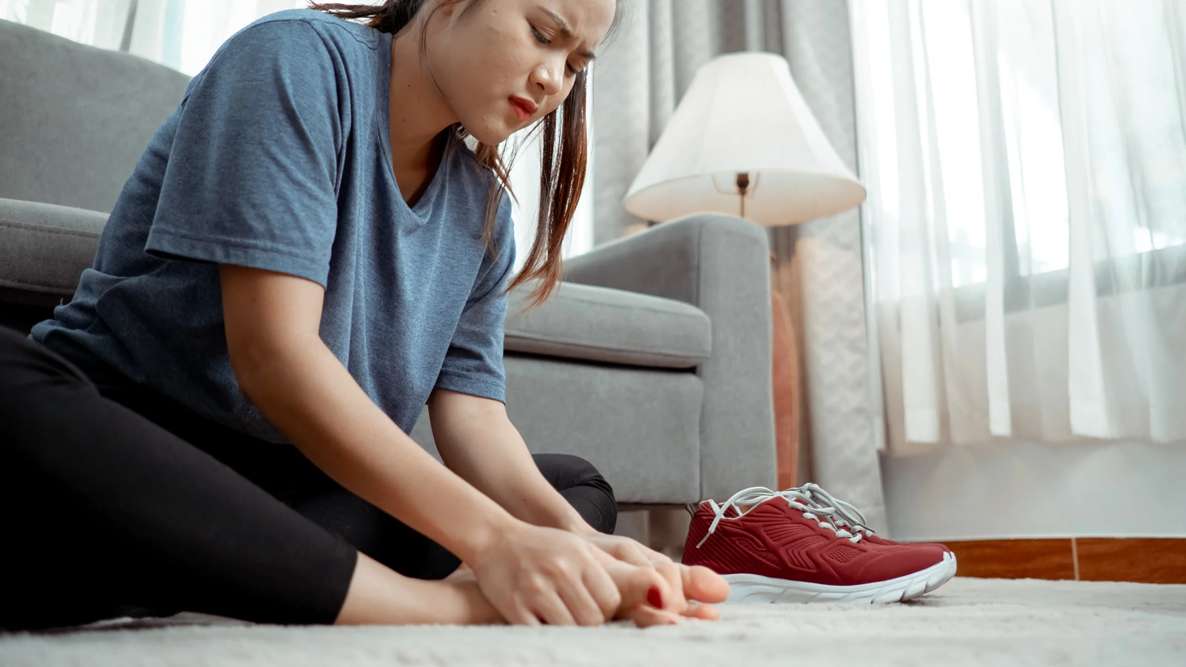 Woman sitting with foot pain at home in the living room.