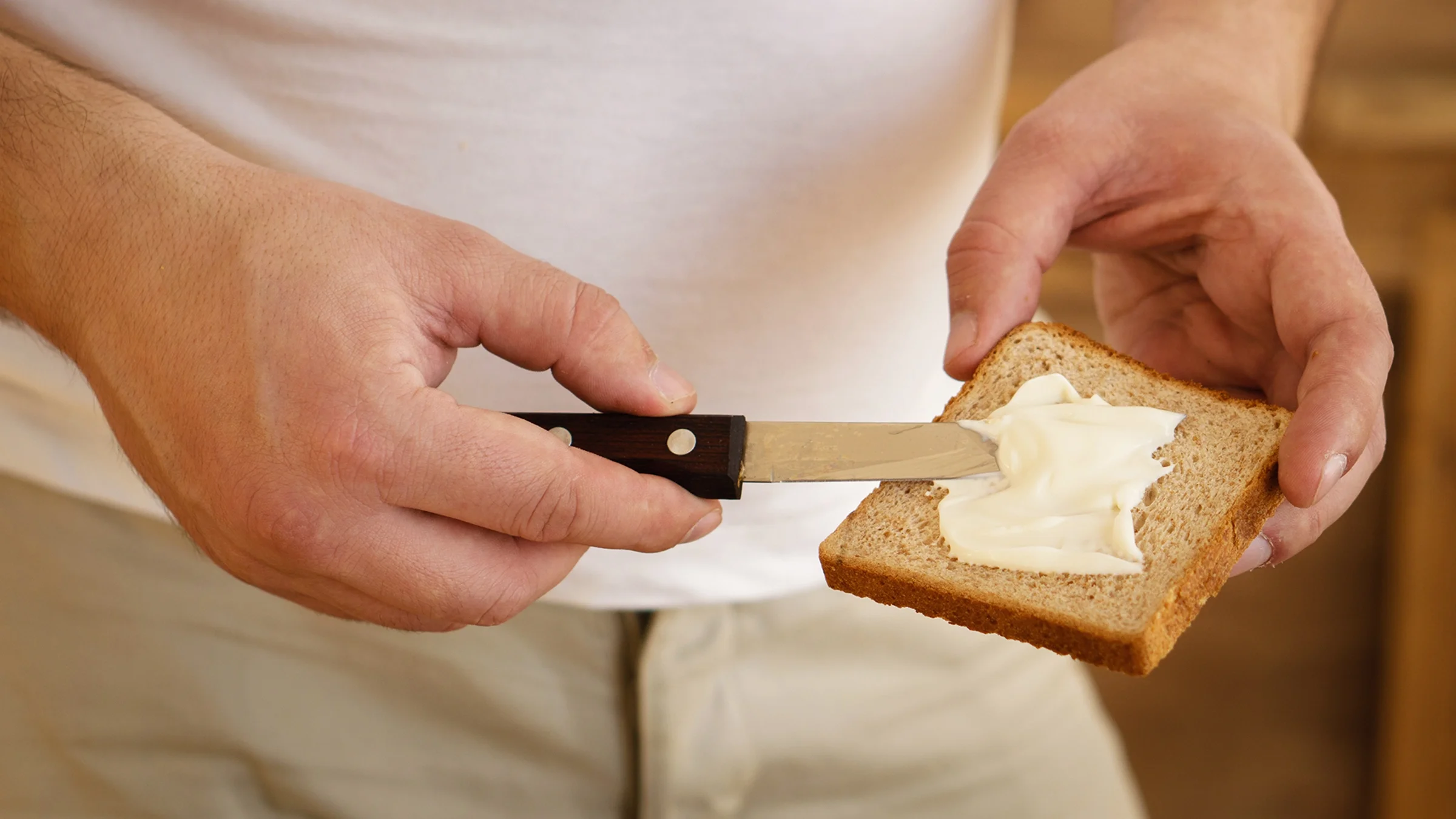 A man spreads mayonnaise on a piece of bread.