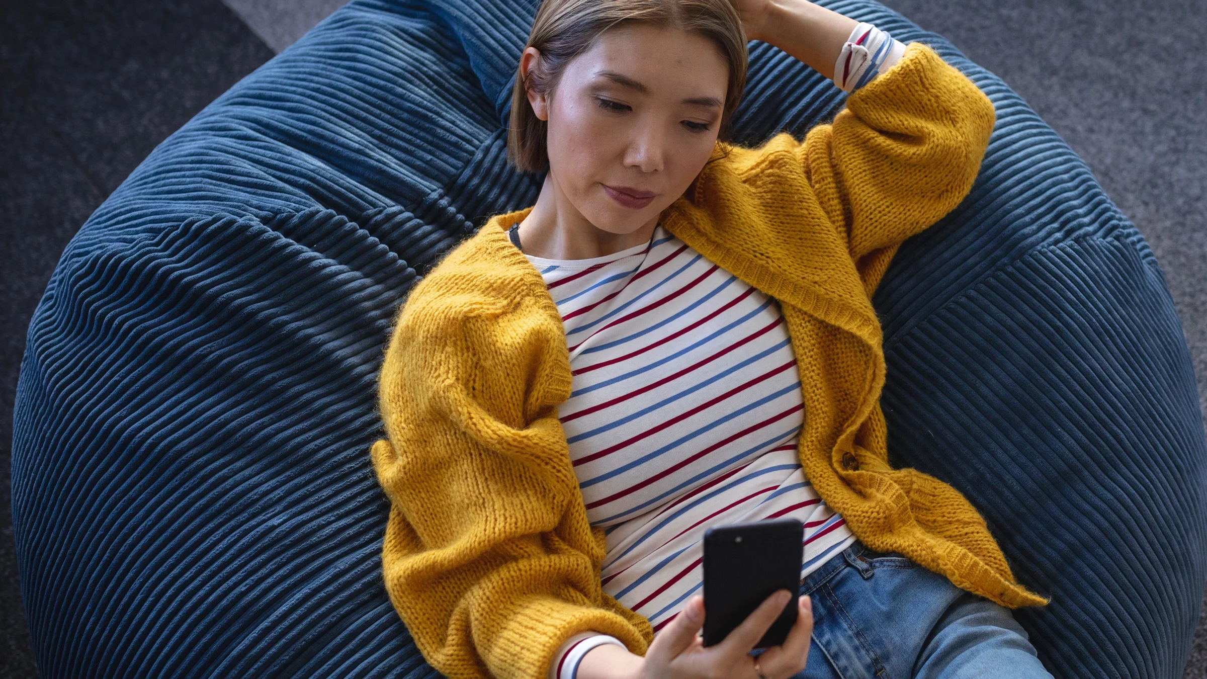 A person using their phone on a bean bag chair.