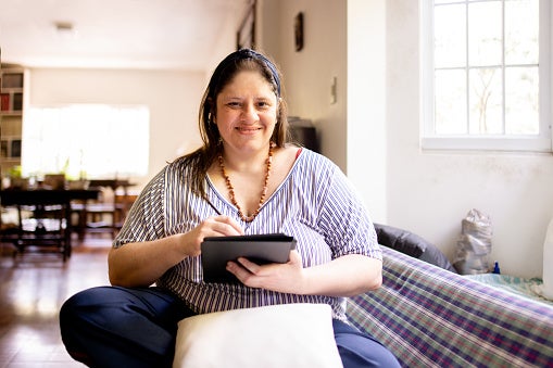Woman sitting crosslegged on couch using her tablet smiling at the camera.
