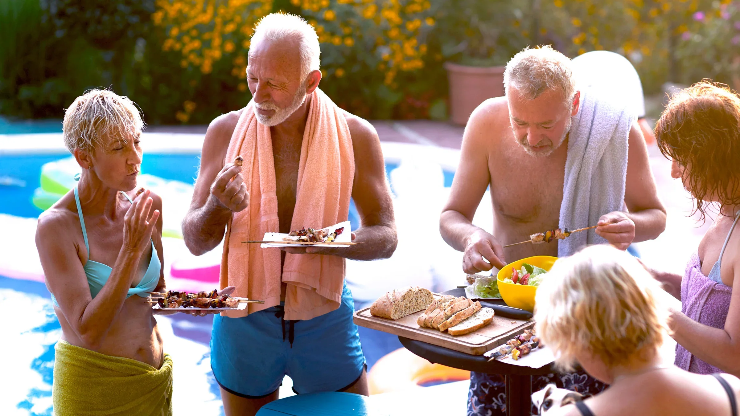 A group of senior friends eating at a pool party.
vgajic/E+ via Getty Images 
