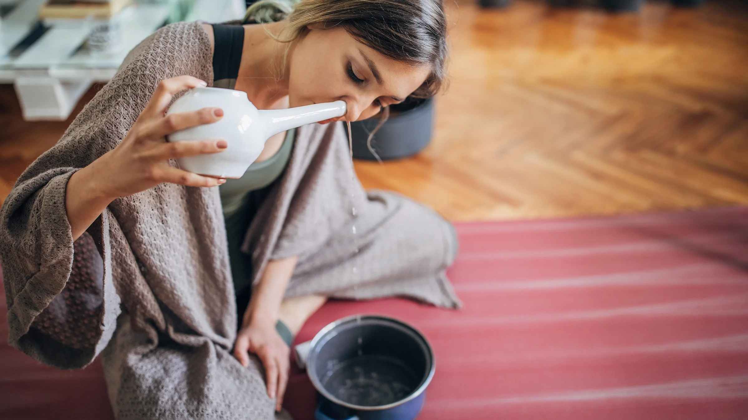 Woman using neti pot while sitting on her yoga mat at home.