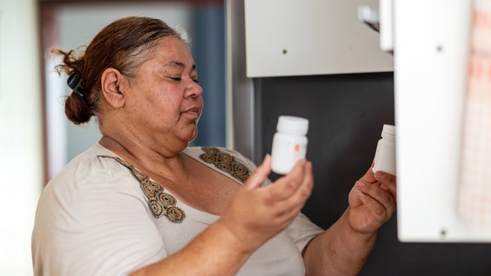 A woman examines medicine bottles in the kitchen.