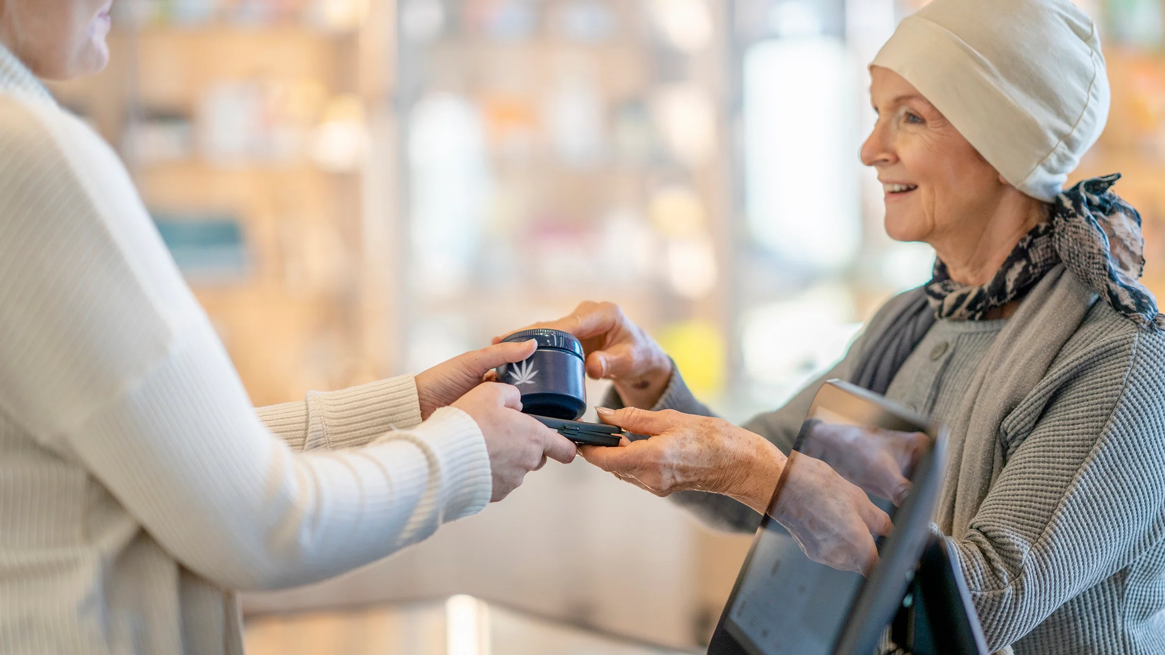 A senior woman with cancer buys cannabis products from someone. The woman is wearing a headscarf.