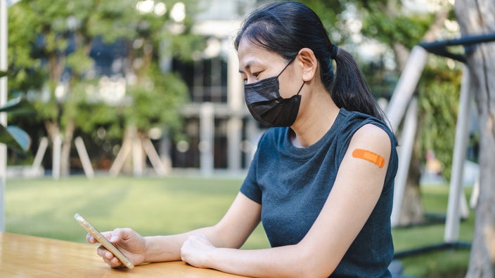 A person with a vaccine bandaid on their arm using their phone. 