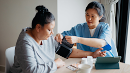 A HCP taking a patient's blood pressure. There are pills on the table.
hxyume/E+ via Getty Images 
