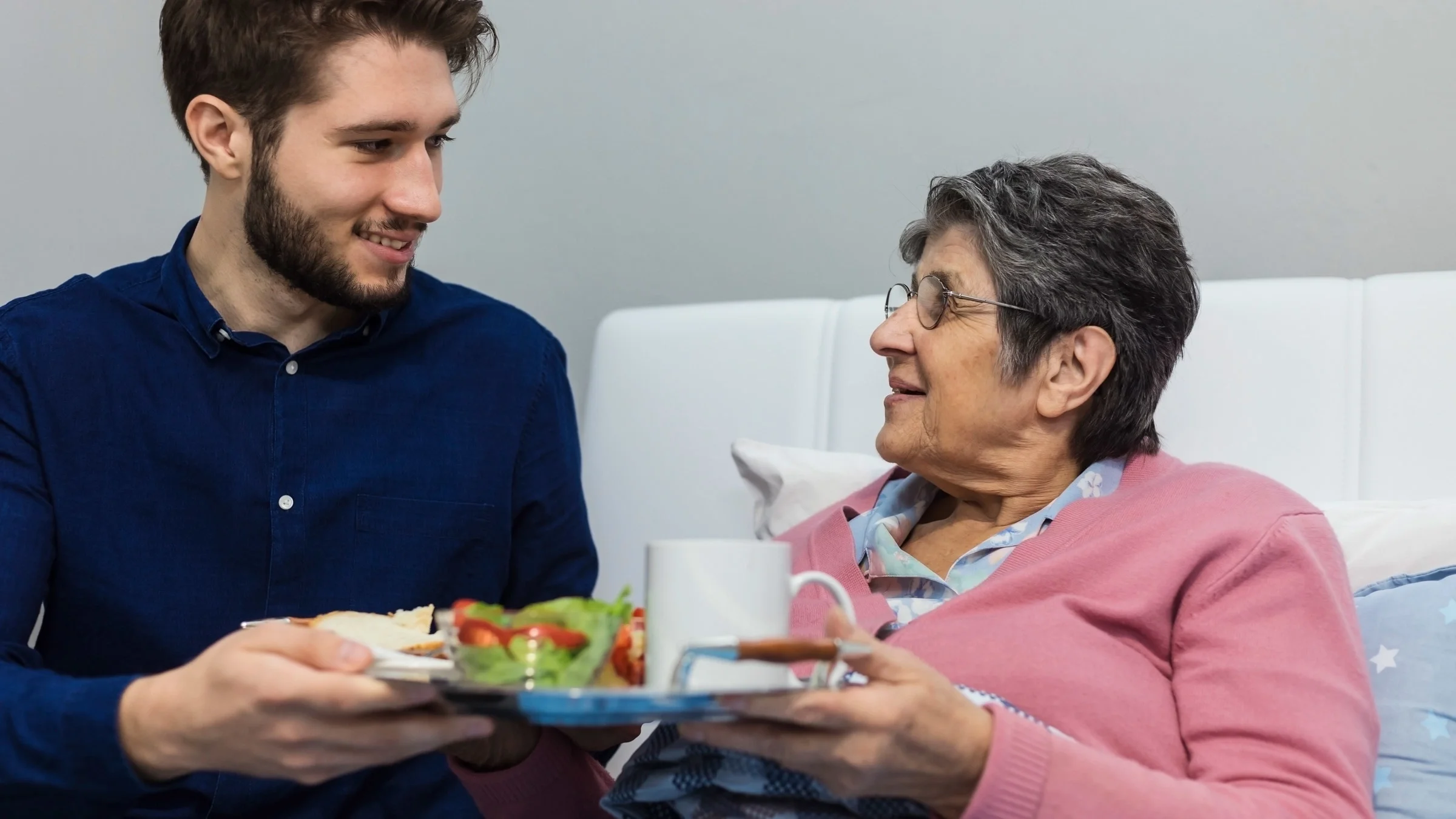 A young adult bringing food to their grandparent in bed.