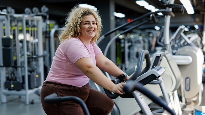 A woman smiles while riding an exercise bike at the gym.