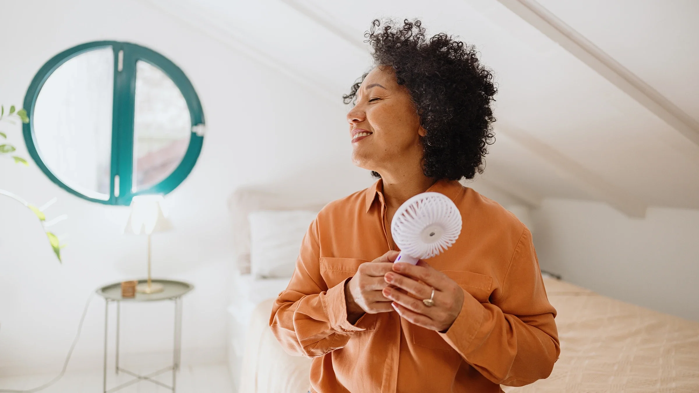 A woman is cooling herself off with a portable fan.