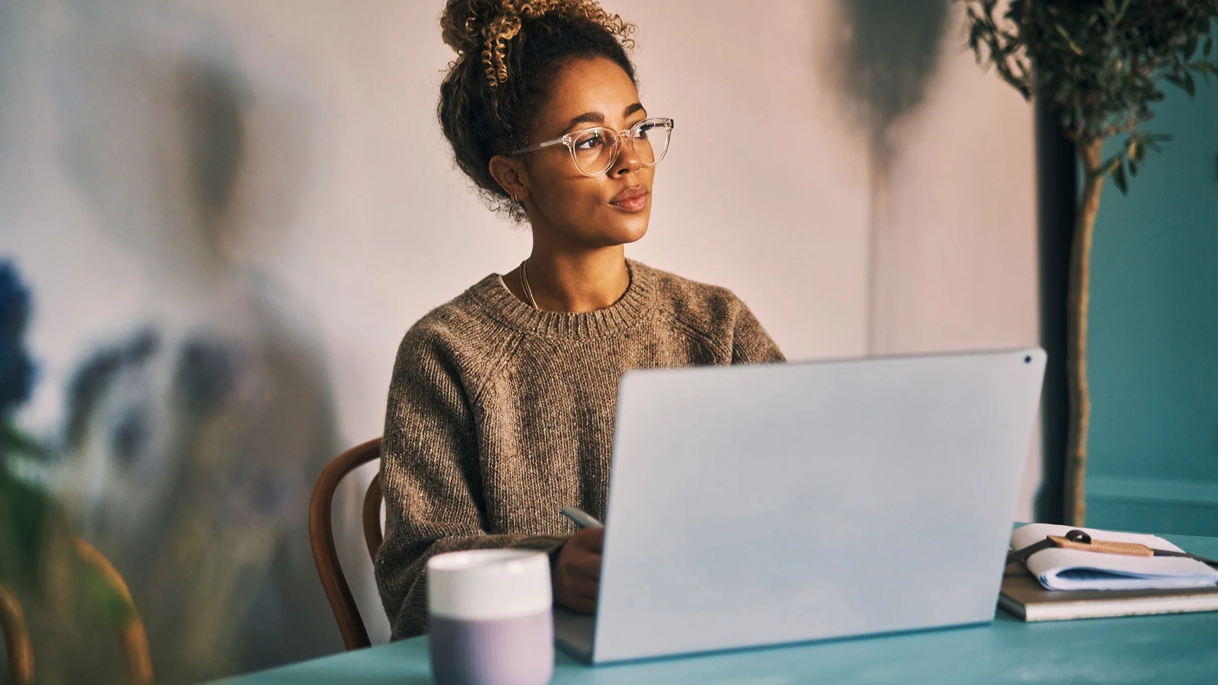 Young woman with her hair up in a bun working at her laptop. She is at an outdoor patio of a coffee shop or restaurant.