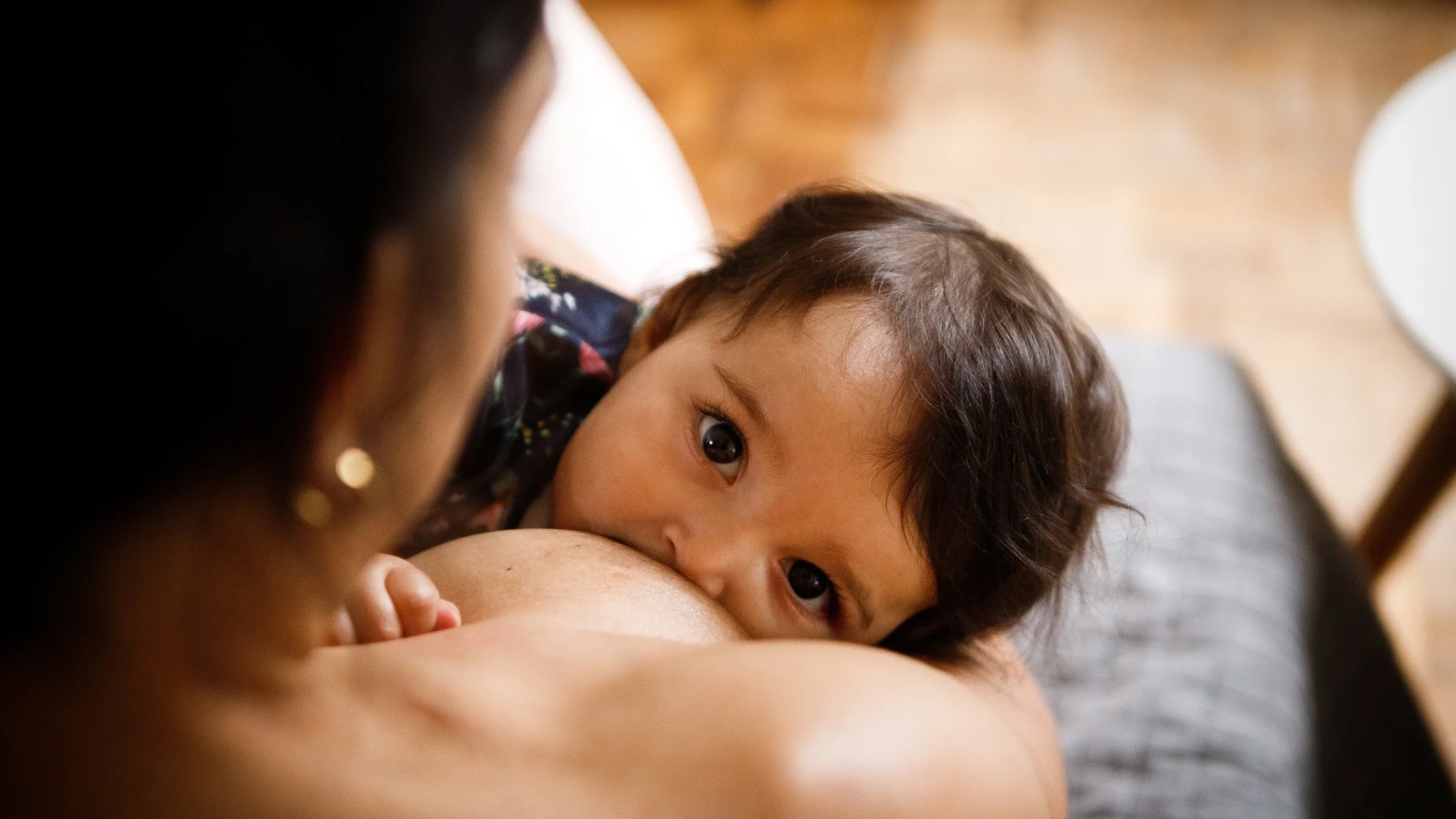 Close-up of a woman breastfeeding her baby who is looking directly up to camera.
