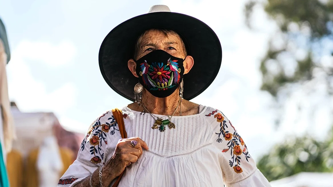 Portrait of an elderly woman wearing an embroidered Mexican blouse and face mask.